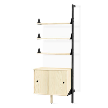 The Gus Modern Branch Storage Unit Add-On is a minimalist wooden wall shelving unit with three open shelves and a two-door cabinet, featuring light wood elements and a black contrasting vertical frame for modular organization.