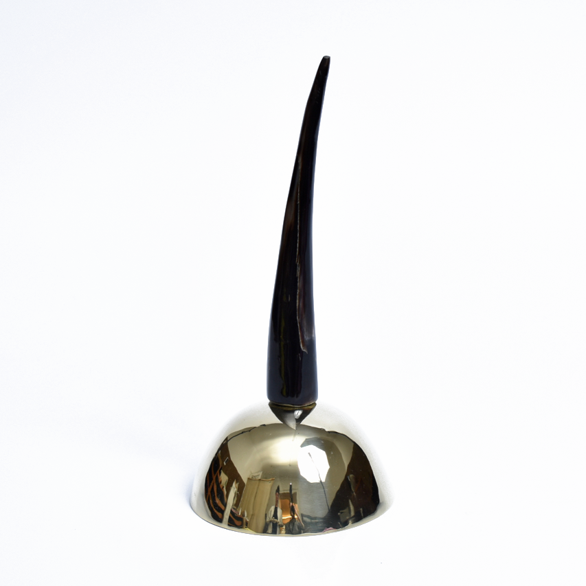 The Bell #3310 by Werkstätte Carl Auböck features a reflective brass cast base with a tall, sleek black spike. This elegant piece evokes the sophisticated design typical of Viennese townhouses, set against a plain white background.