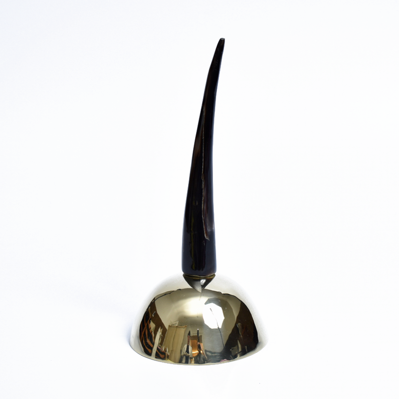 The Bell #3310 by Werkstätte Carl Auböck features a reflective brass cast base with a tall, sleek black spike. This elegant piece evokes the sophisticated design typical of Viennese townhouses, set against a plain white background.