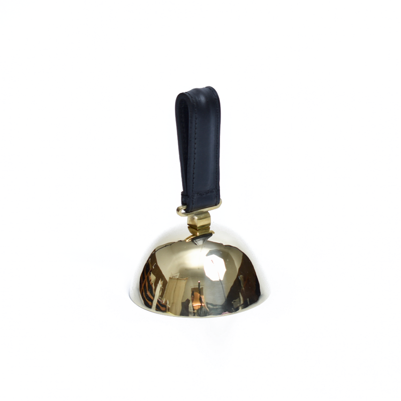 Bell #3310 by Werkstätte Carl Auböck features a polished brass surface and a sleek black leather handle. Photographed against a plain white background, its reflective surface subtly mirrors its surroundings, reminiscent of the elegance in a Viennese townhouse.