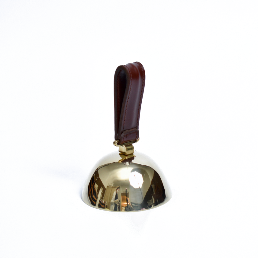 Bell #3310 by Werkstätte Carl Auböck, featuring a brown leather handle on a white background, showcases a shiny brass craftsmanship reminiscent of Viennese townhouse designs with its reflective surface and echoes Carl Auböcks iconic style.