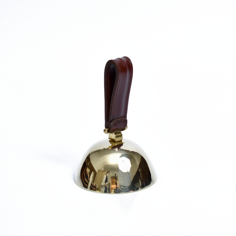 Bell #3310 by Werkstätte Carl Auböck, featuring a brown leather handle on a white background, showcases a shiny brass craftsmanship reminiscent of Viennese townhouse designs with its reflective surface and echoes Carl Auböcks iconic style.