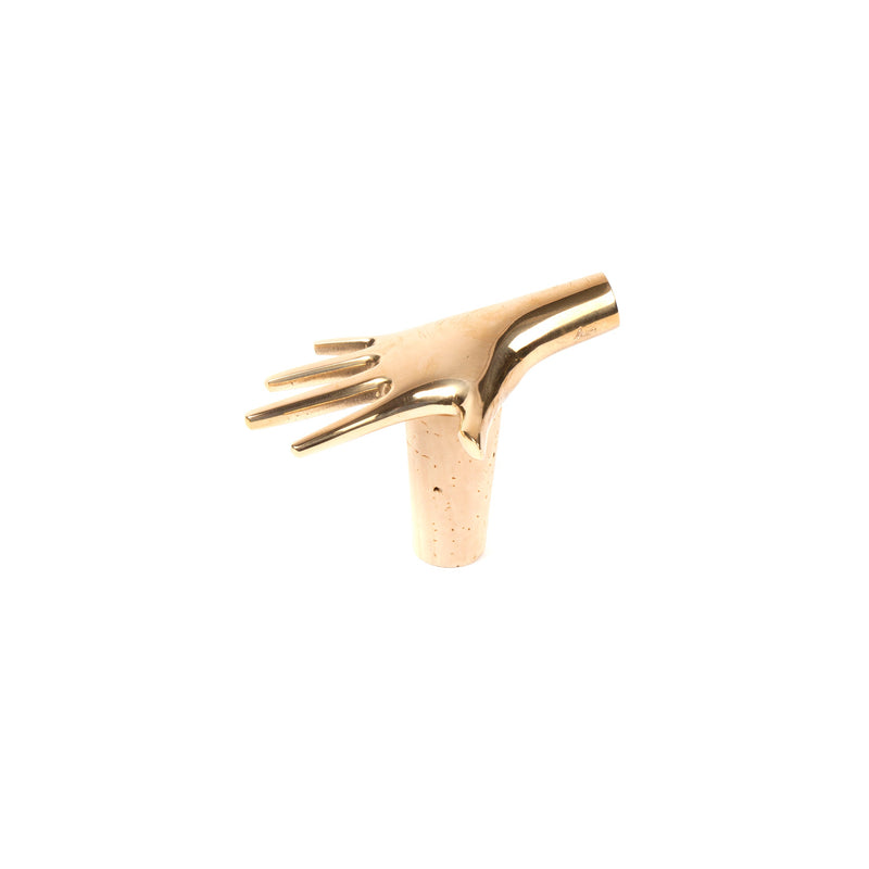 The Werkstätte Carl Auböck Corkstopper Palm #4220 is a minimalist sculpture resembling a golden hand with extended fingers. Its smooth, reflective surface evokes the elegance of a Viennese townhouse, set against a plain white background.