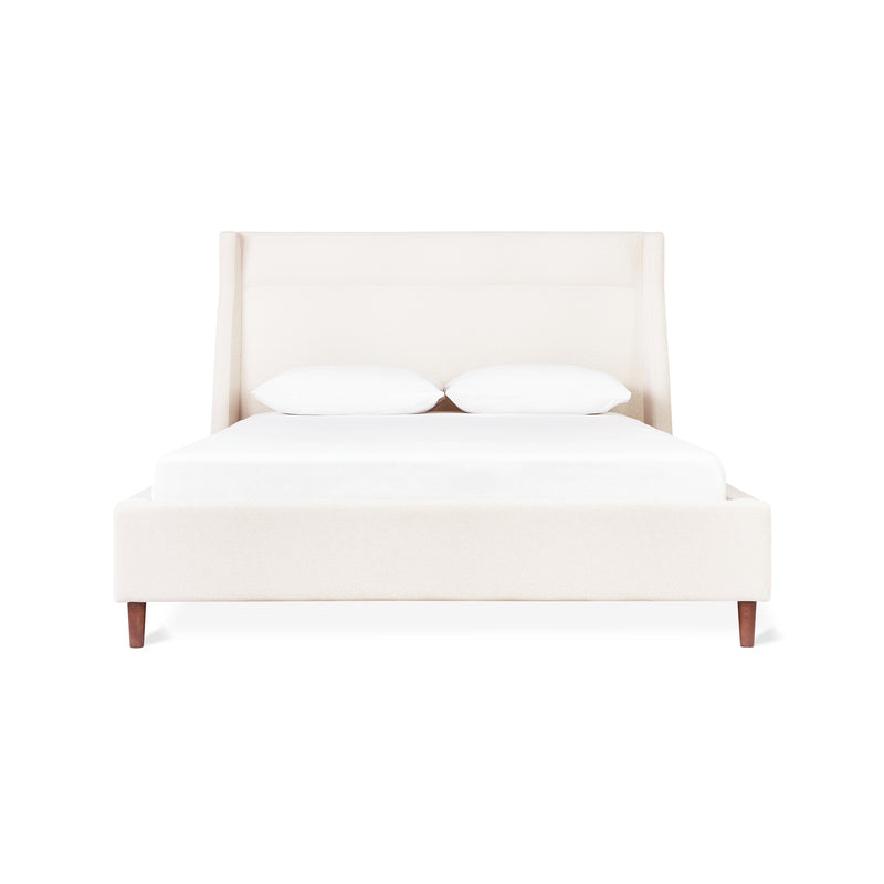 The Gus Modern Carmichael Bed features cream upholstery, a tall headboard, white bedding, and two pillows—all shown front-facing against a white background.