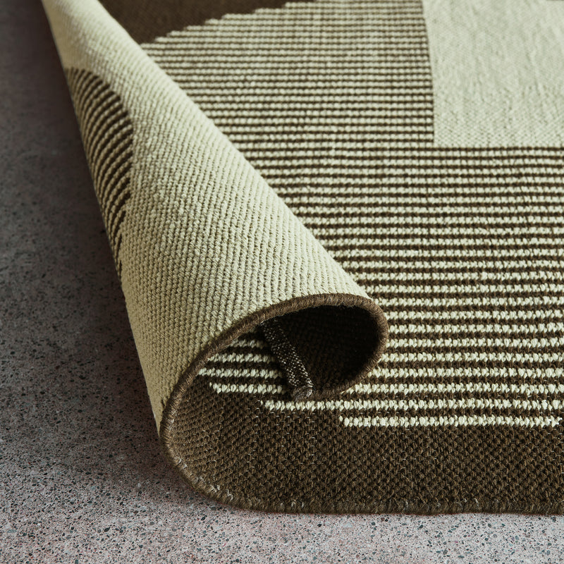 Close-up of a beige and brown woven rug with a folded corner showing striped and solid textured patterns