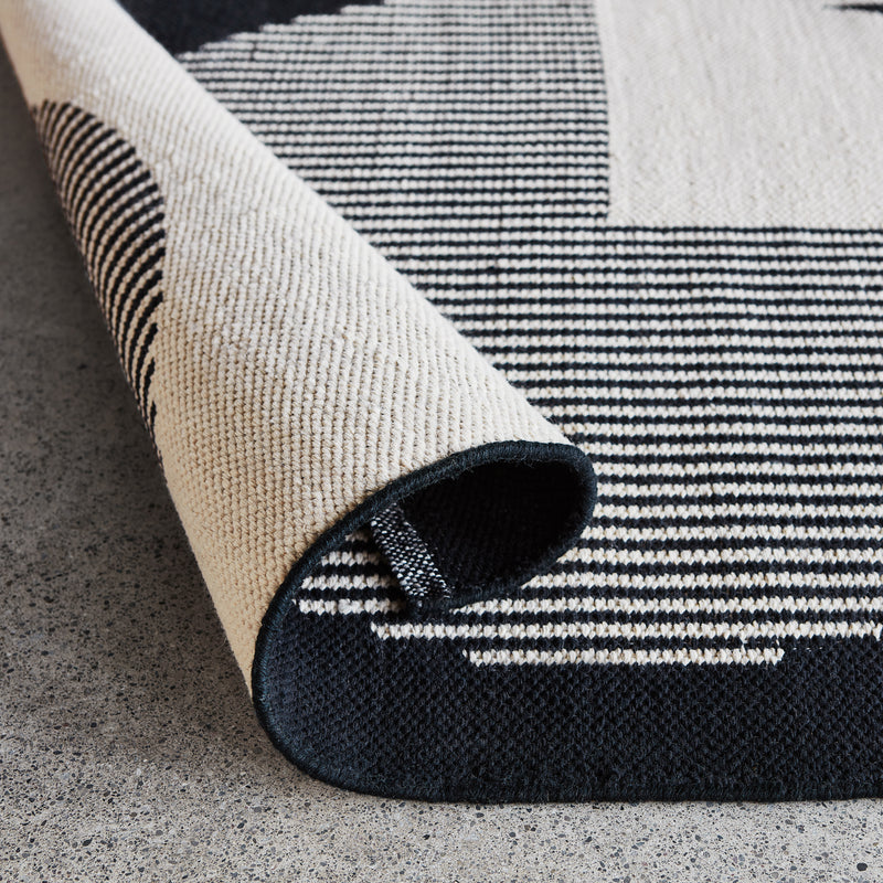 Close-up of a folded beige rug with black striped geometric pattern on a textured concrete floor