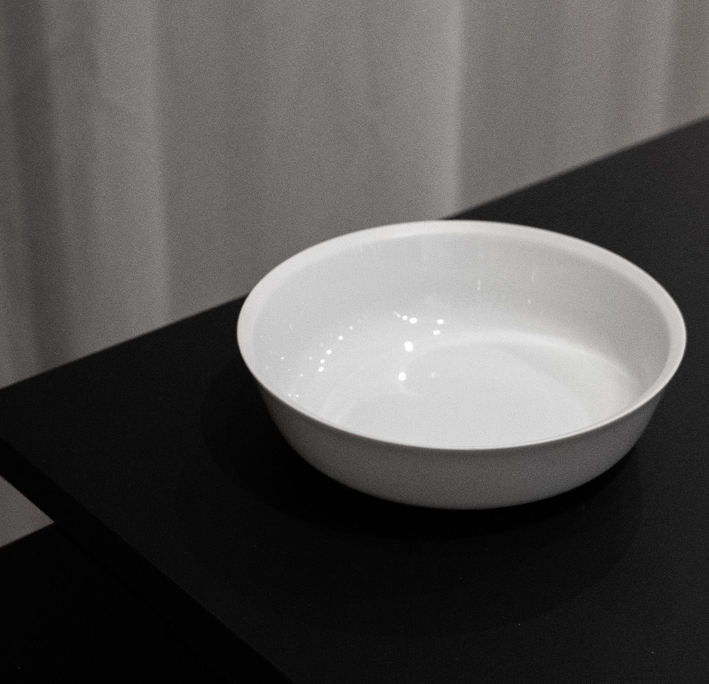 The Augarten Orbit Collection - Sale features a white ceramic bowl crafted with exquisite precision, sitting on a black surface. Its glossy finish and subtle rotational shapes highlight its elegance, making it a sophisticated addition to any table setting.