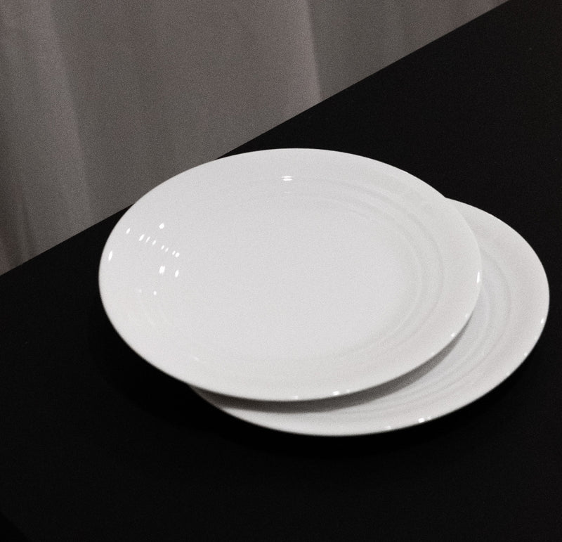 Two white Augarten Opus Collection plates, reminiscent of Vienna Porcelain, are elegantly stacked on a black tablecloth set against a soft-focus gray curtain backdrop.