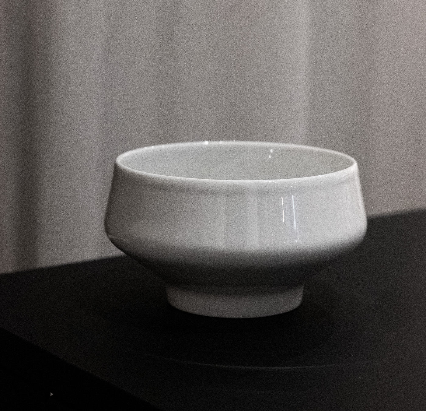 The Augarten Shortcut - Sale white porcelain bowl, with a subtle glossy finish, rests on a dark surface against a softly blurred, neutral background, highlighting the timeless elegance of Augarten craftsmanship.
