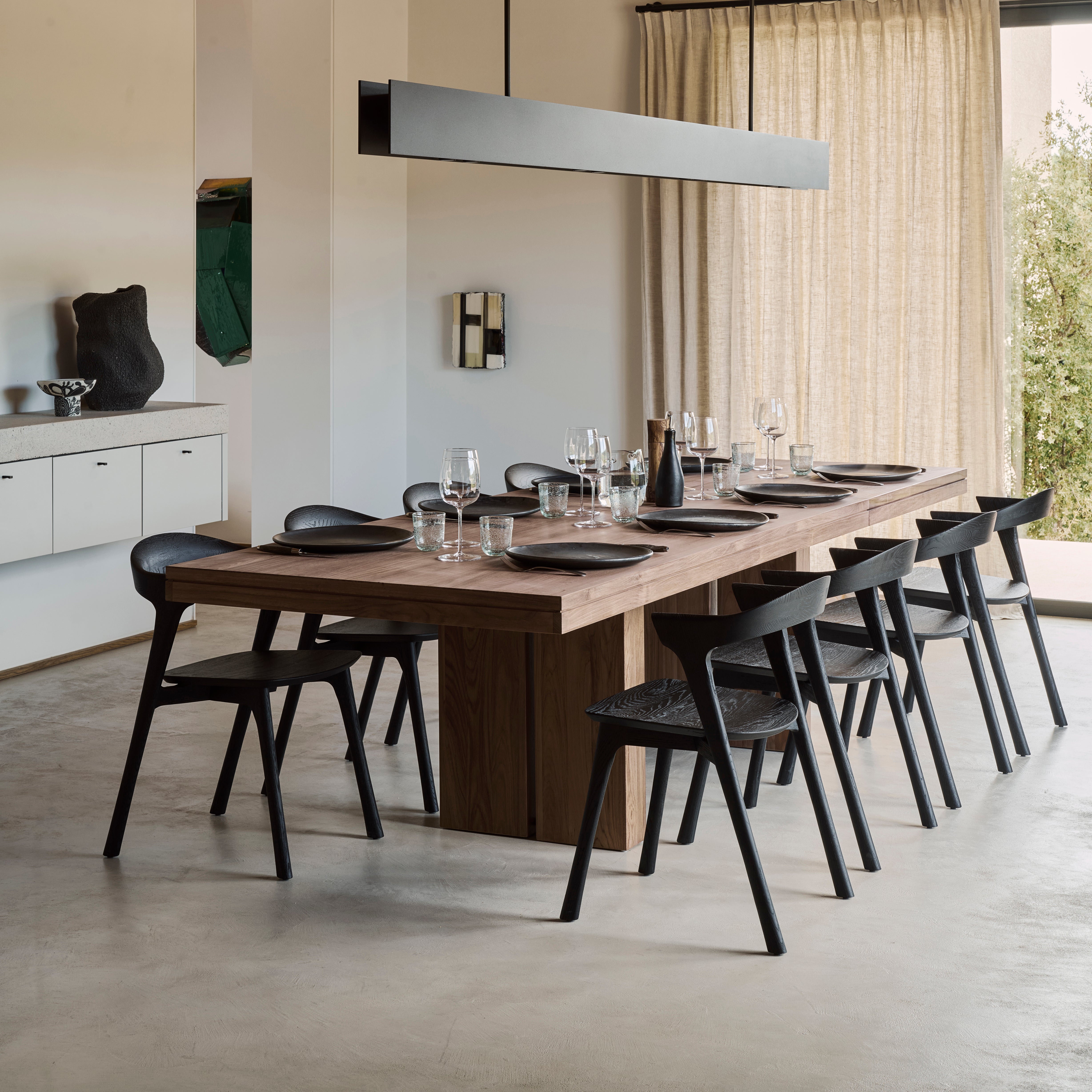 Double Extendable Dining Table by Ethnicraft in teak, showing extended length with modern black chairs and table setting.