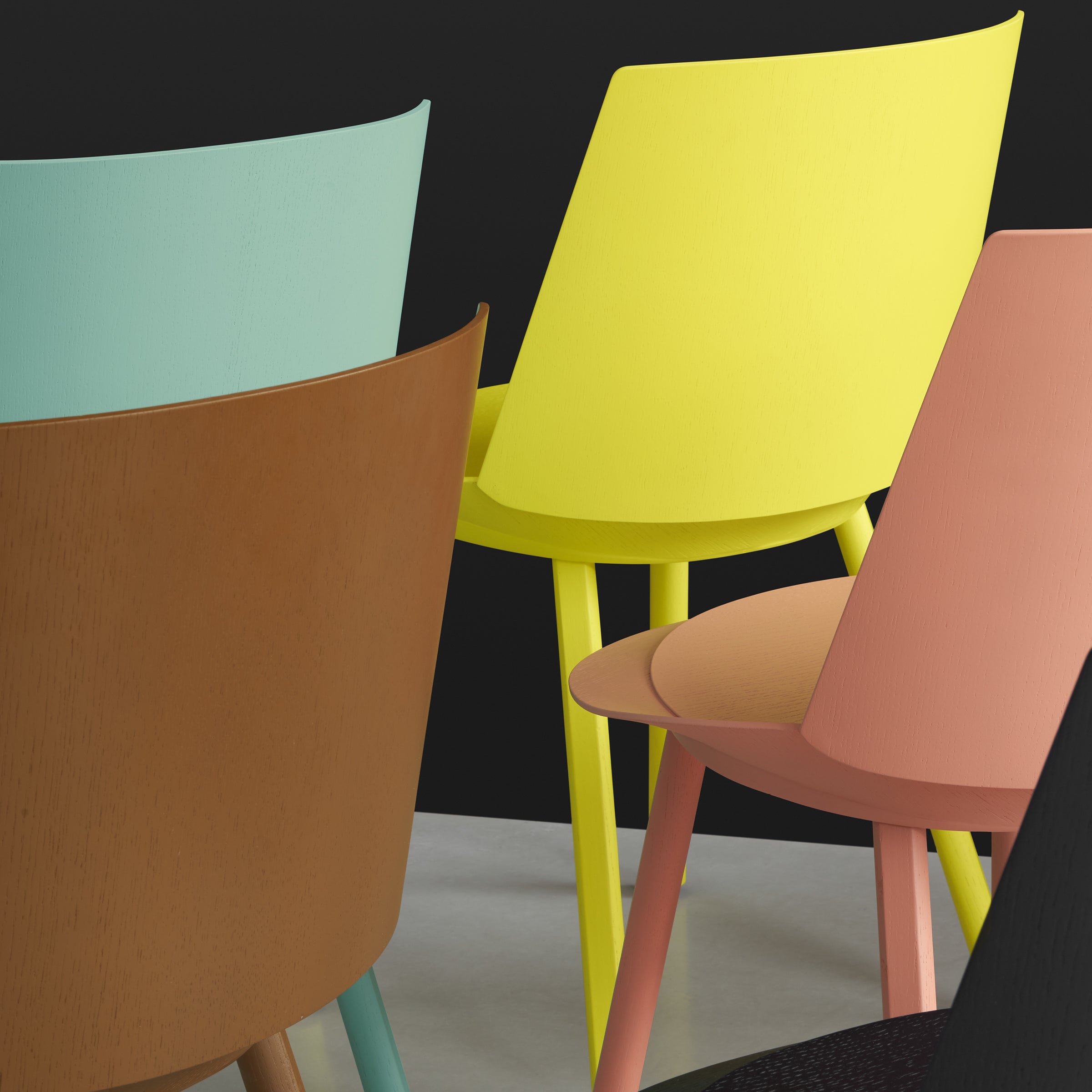 A collection of modern chairs is exhibited, featuring the sleek CH04 HOUDINI by E15 and designs by Stefan Diez. Available in vibrant yellow, pink, and light blue, these chairs highlight their minimalist appeal against a dark backdrop when placed closely together.