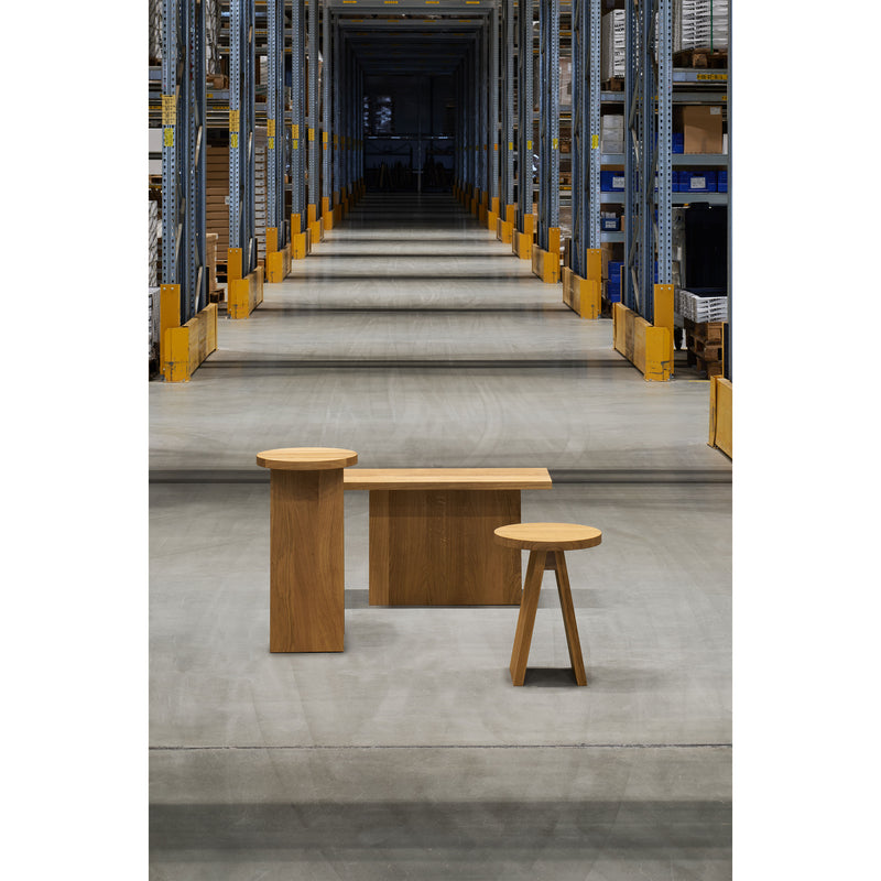 A modern, minimalist bench and a European E15 EK01/EK02 Stool set are placed in the foreground of a spacious warehouse aisle. The shelving units stretch into the distance, adding subtle elegance to the industrial setting.