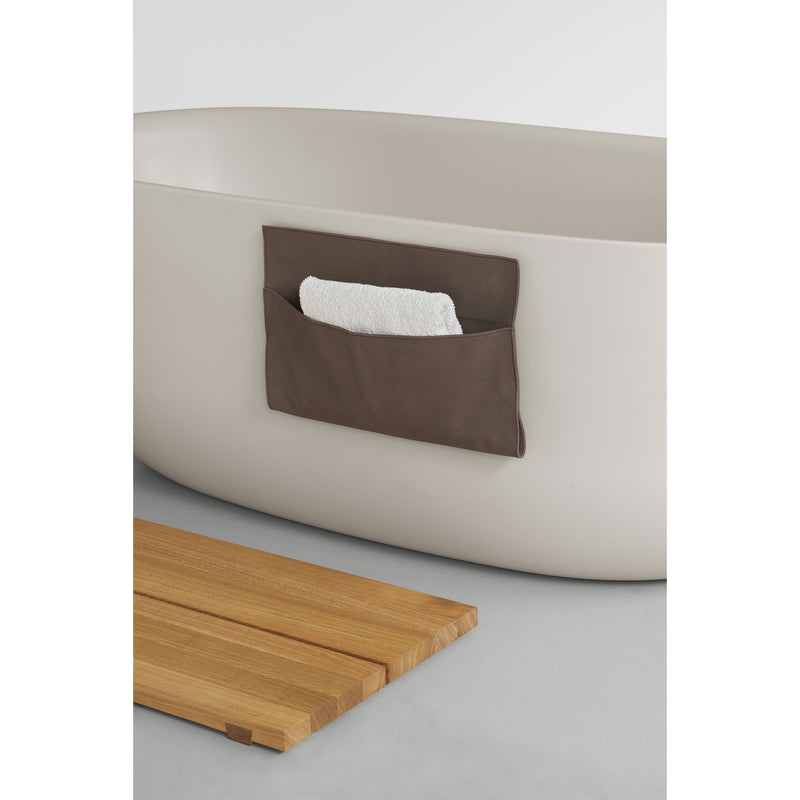 The EK06 Base by E15, a freestanding white bathtub, includes a brown pouch with a folded white towel and is enhanced by a European oak bath mat on the gray floor for a simple, spa-like ambiance.