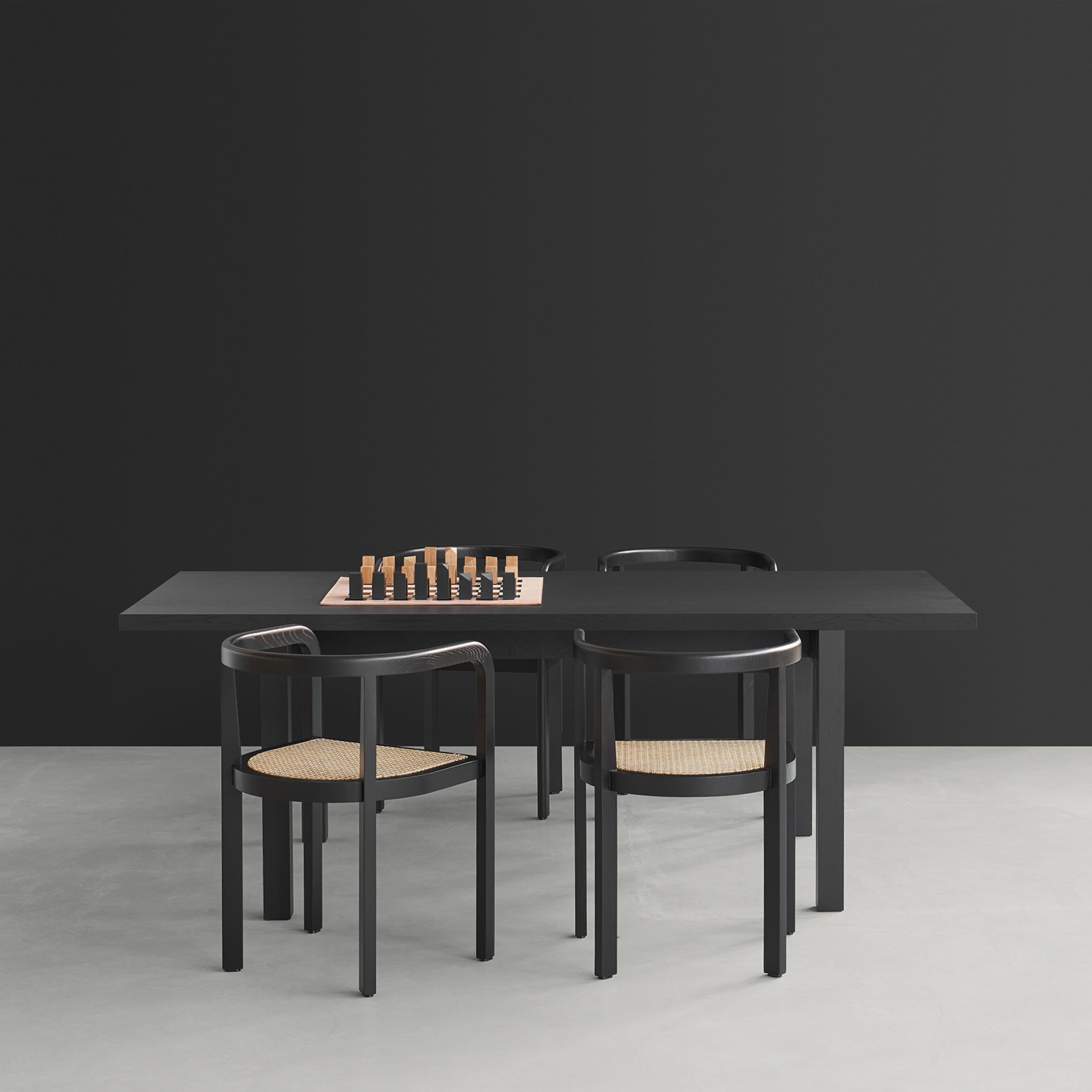 A sleek, modern black dining table from E15 with four chic RH01 Stuttgart chairs boasts a chessboard center that showcases solid wood craftsmanship, perfectly complementing a minimalist room with dark walls and light floors.