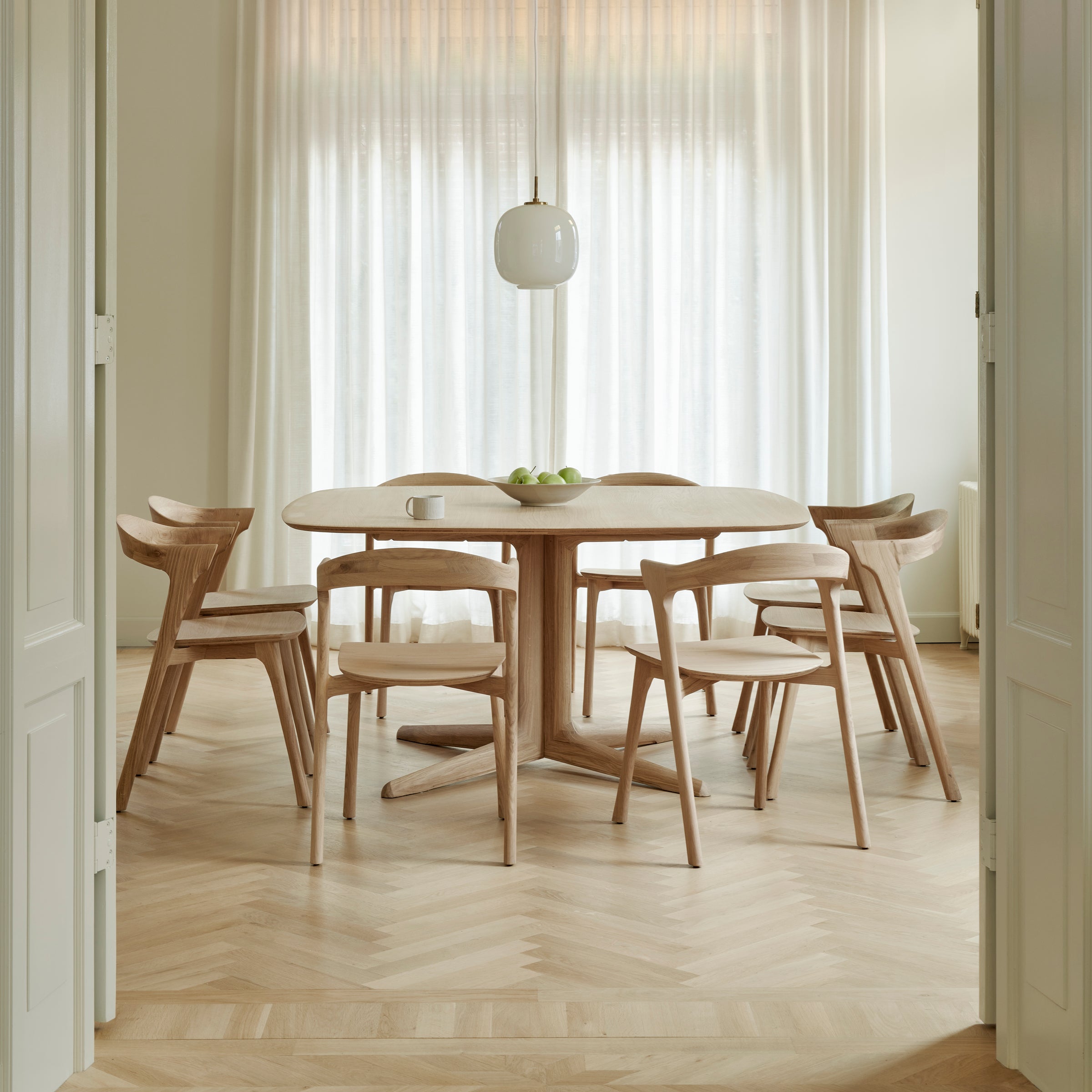 Bok Dining Chair set around a modern wooden dining table in a bright, minimalist room with sheer curtains.