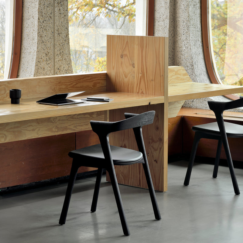 Bok Dining Chair in black varnished oak with ergonomic design, stylish and modern, placed by wooden desk in natural light room.