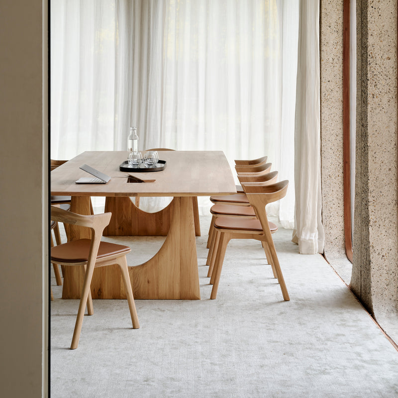 Bok Dining Chair - Upholstered in varnished oak and cognac leather around a modern wood dining table in a bright room.