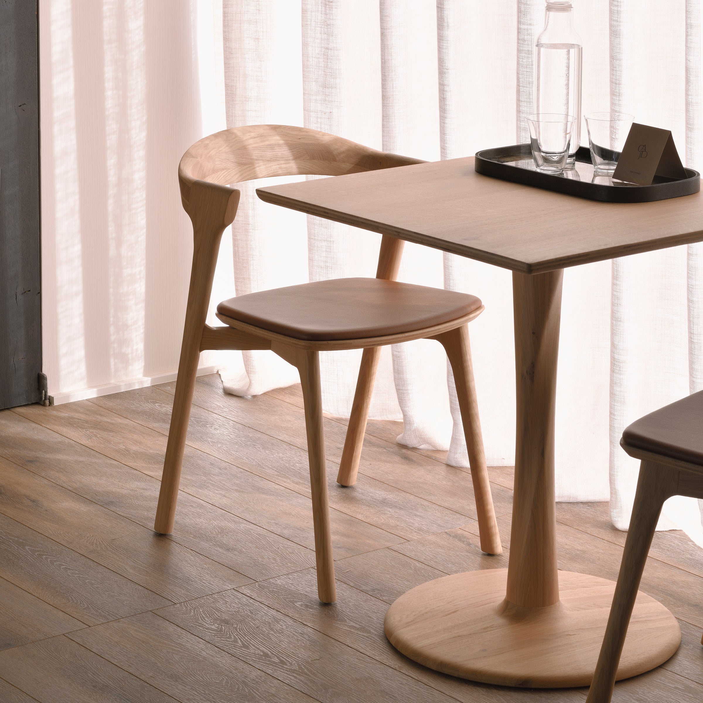 Bok Dining Chair - Upholstered in warm varnished oak and leather beside a matching wooden dining table.
