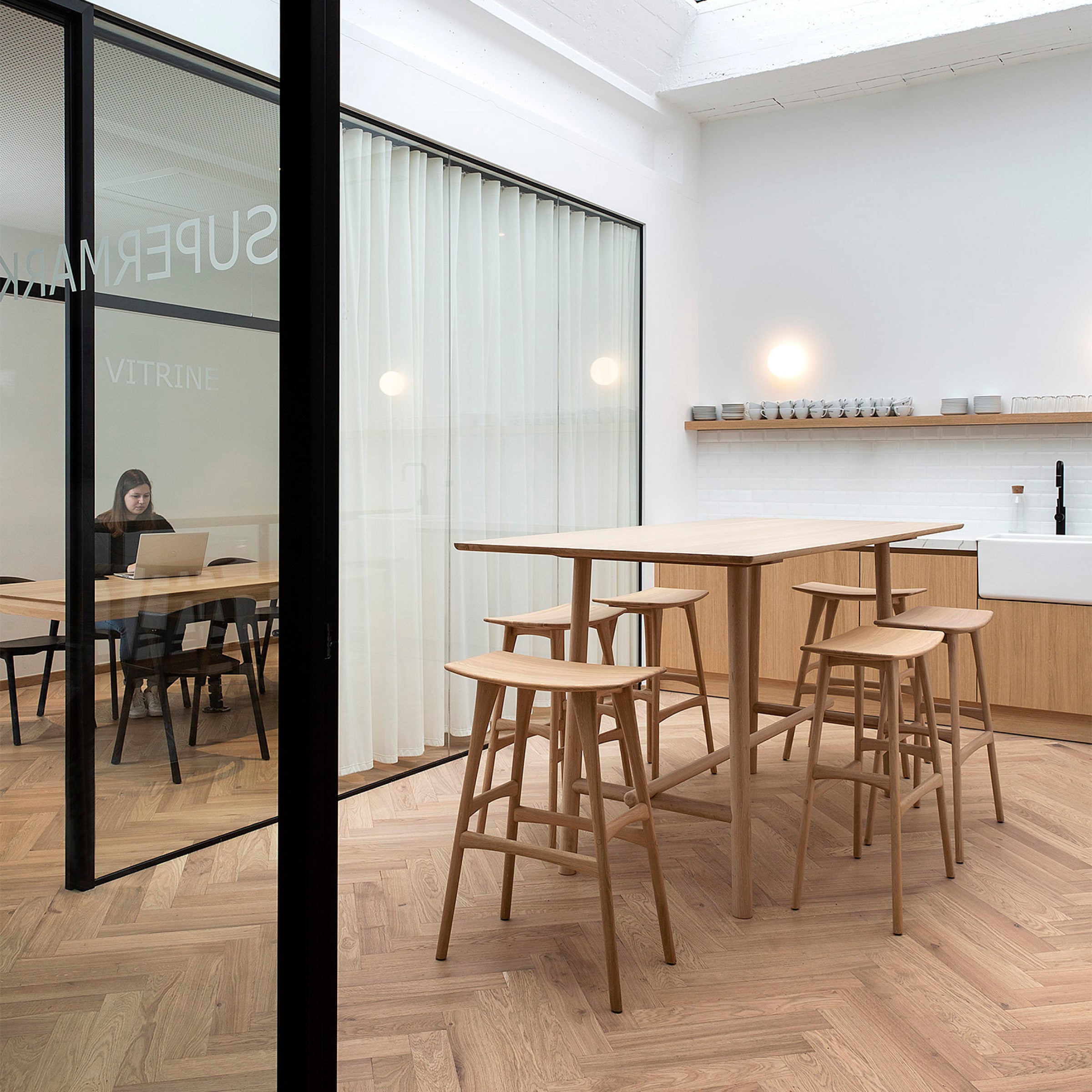 Osso Bar Stool set around a high wooden table in a modern minimalist kitchen with oak flooring.
