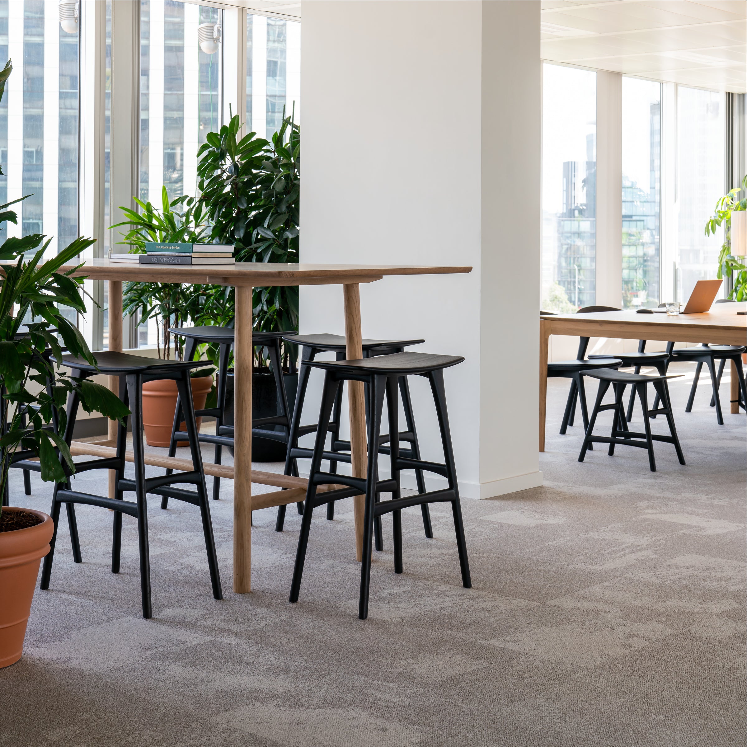 Osso Counter Stool in black varnished oak with a minimal design around a wooden high table in a bright office space.