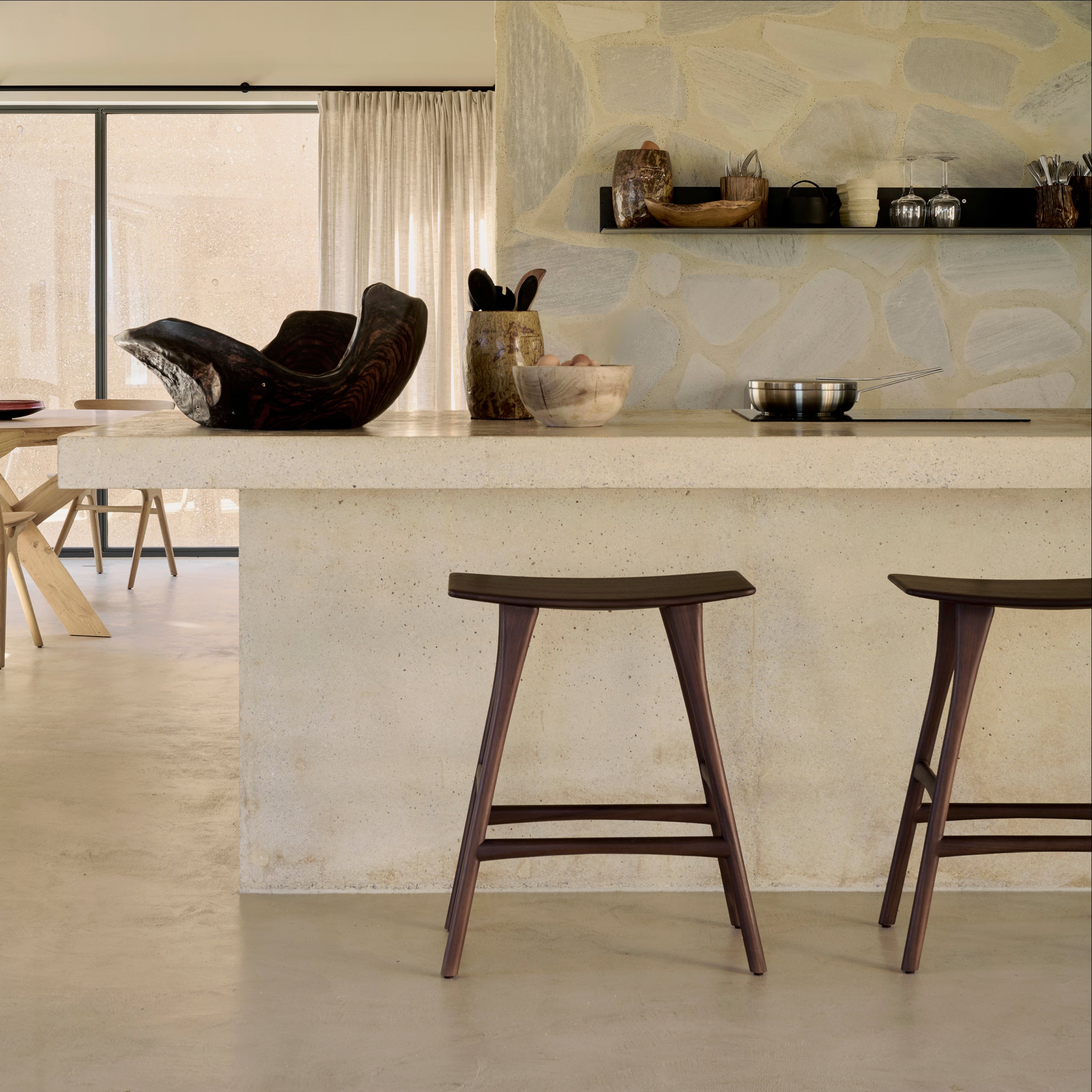 Osso Counter Stool in dark wood with curved seat, placed at a beige kitchen island in a modern home.