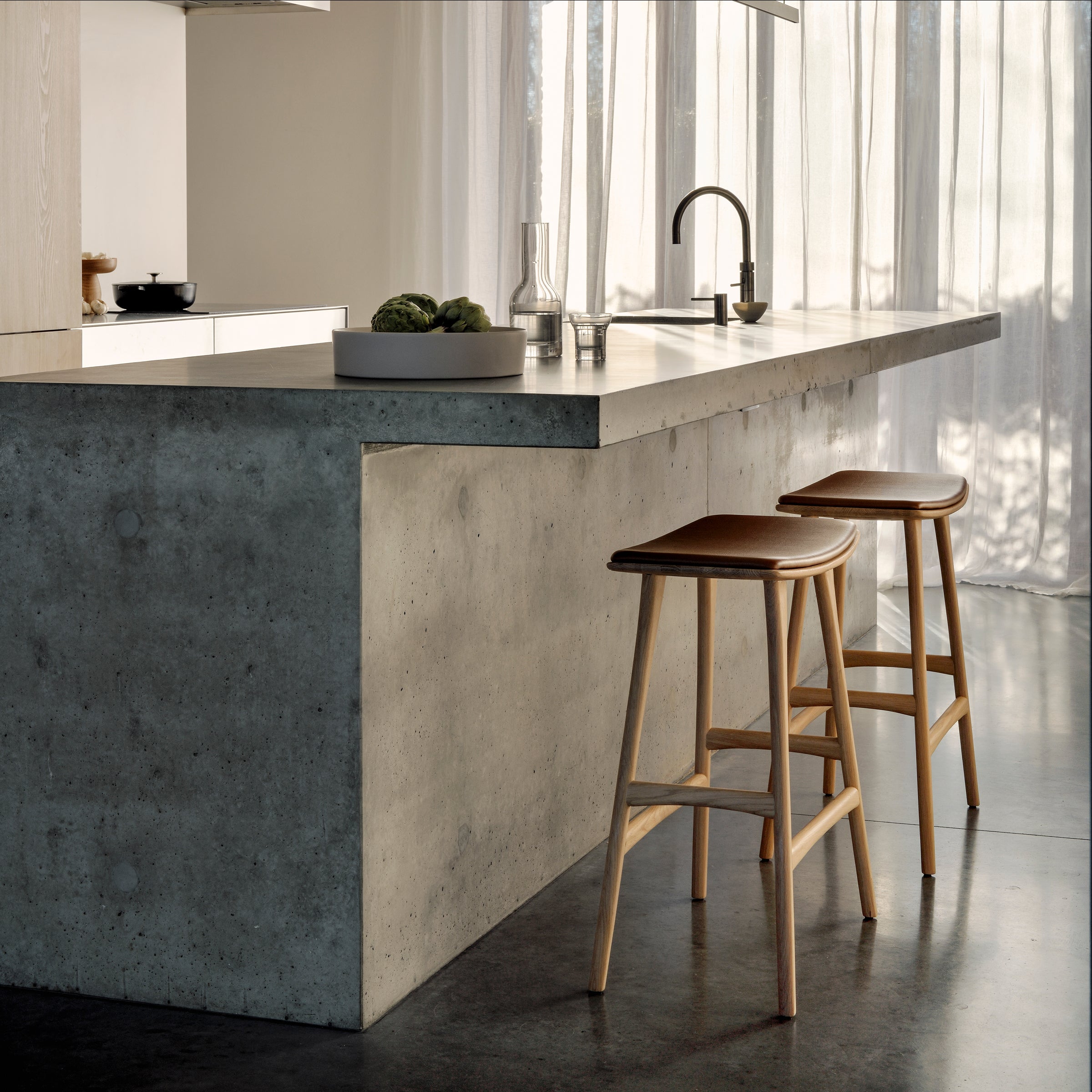 Osso Counter Stool made of solid oak with cognac leather upholstery placed beside a modern kitchen island.