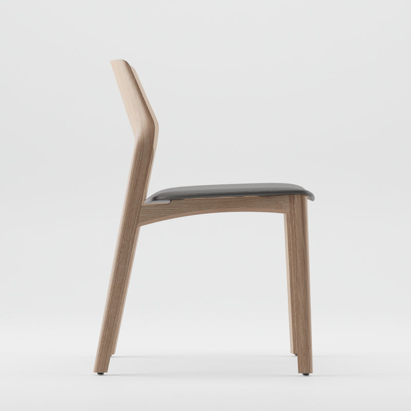 The FIN Chair Upholstered by Artisan features a minimalist design with a solid wood frame finished in natural oils and a dark cushioned seat. It boasts an eco-friendly design, straight backrest, and simple elegance, all set against a plain white background.
