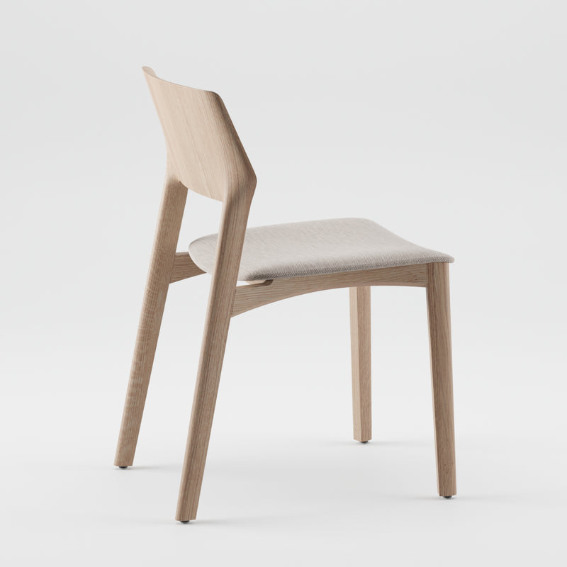 The FIN Chair Upholstered by Artisan is a modern wooden chair crafted from solid wood and natural oils. It features a minimalist design with clean lines, an angled backrest, and a light fabric seat, all set against a plain white background.