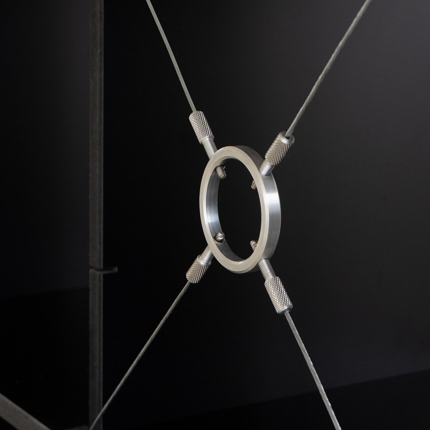 On a dark background, the FNP by Moormann showcases an adjustable design with a metal ring suspended by four cables arranged in an X shape, screwed into place.