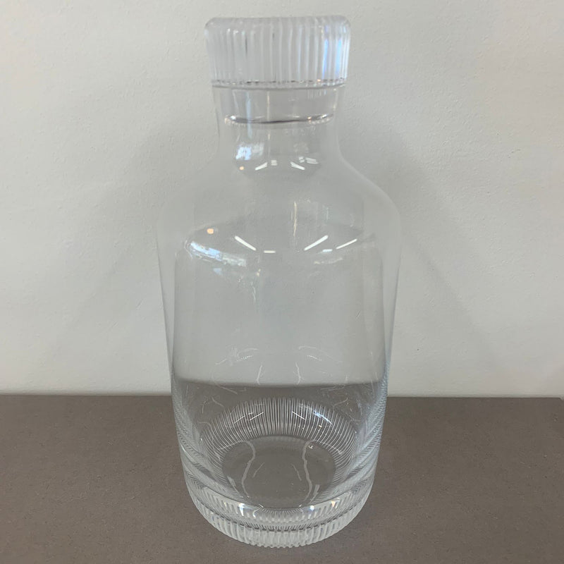 A clear glass bottle from Lobmeyrs Drinking Set No. 281 - Grip - Sale, featuring a ridged cap, rests on a gray surface against a light background. This empty whiskey decanter is crafted from mouth-blown lead-free crystal, highlighting its transparent material and elegant design.