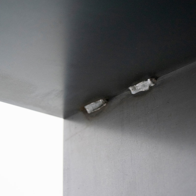 Close-up of a corner of a metallic structure, featuring two weld spots joining steel plates, reminiscent of Moormanns precise Gespanntes Regal craftsmanship. The surface is smooth and reflective, with a shadow along the inner edges, highlighting the industrial design.