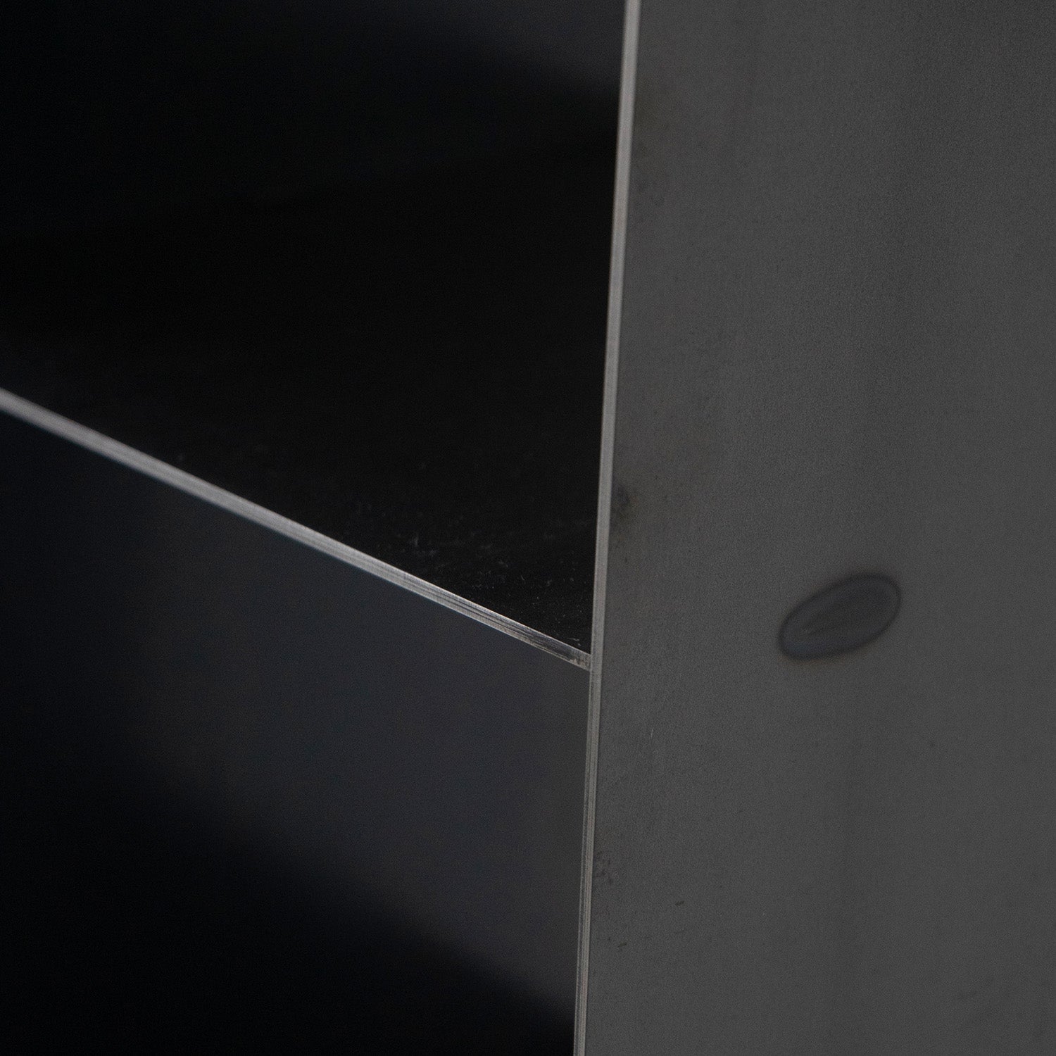 Close-up of the Gespanntes Regal by Moormann, showcasing a dark surface with precision edges and a circular side indentation, reminiscent of Nils Holger Moormanns style, seen in soft light.