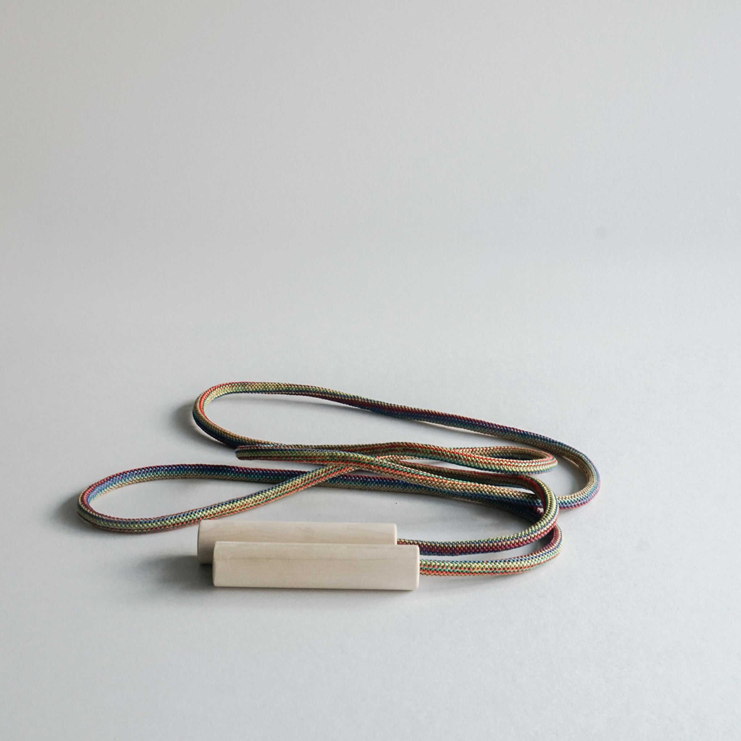 A GoodGoods Spring skipping rope, L 86.6, showcases a vibrant ash and rope design with wooden handles, resting elegantly on a plain white surface as its multi-colored rings form neat patterns inviting kids to play.