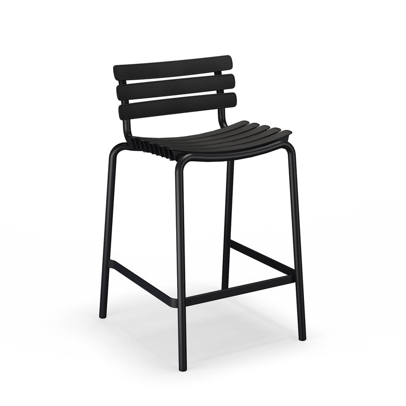 The ReClips Counter Chair by Houe is a black, minimalist bar stool featuring a sleek design with a slatted backrest, four slender legs with a square footrest, and a curved seat, all crafted from powder-coated aluminum for modern elegance.