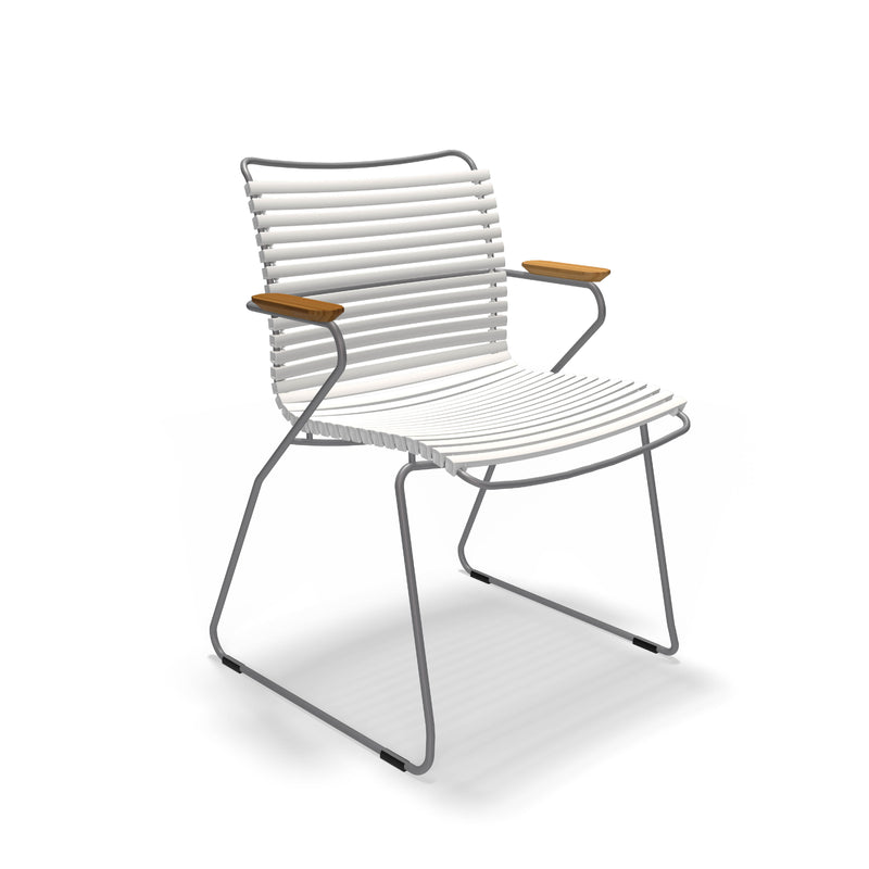 The Click Dining Chair with Armrest by Houe is a modern outdoor chair with a minimalist design, featuring a weather-resistant white ribbed seat and backrest, silver metal frame, and wooden armrests. Its sled-style base adds to its sleek look, perfect for stylish alfresco settings.