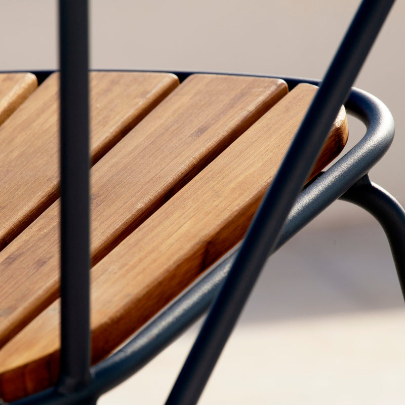 A close-up of the Houe Paon Rocking Chair displays bamboo lamellas and a sleek, powder-coated steel frame. The angled shot highlights the contrast between the warm bamboo and cool metal on a neutral backdrop.