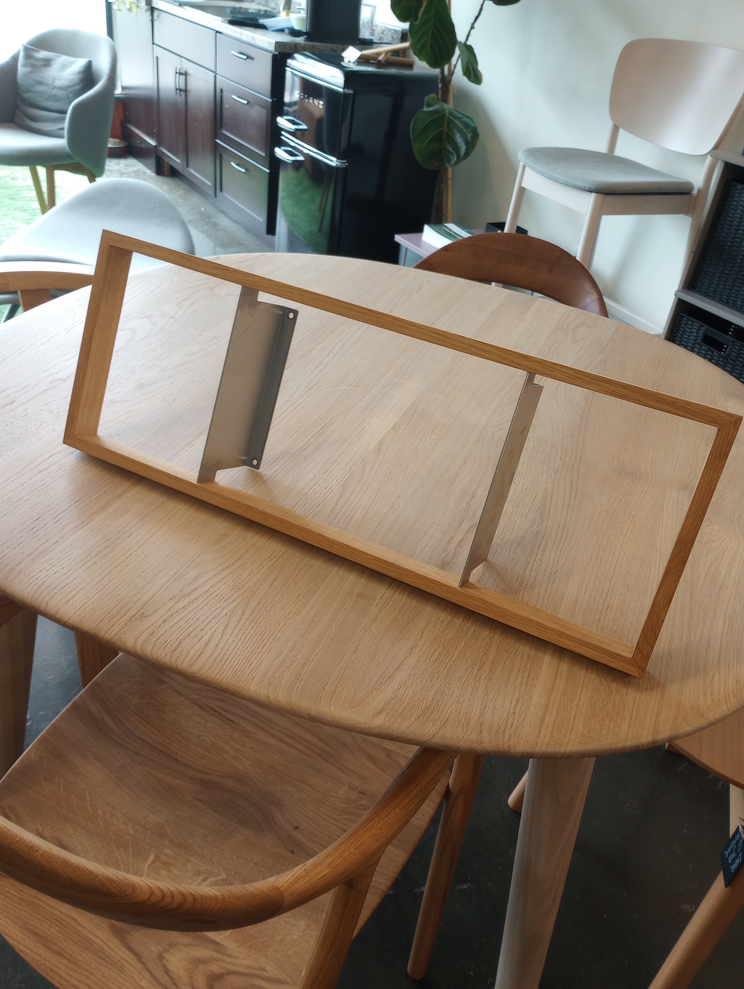 A solid wooden frame with metal slots sits on a round wooden table surrounded by chairs. In the background, floating bookshelves and additional seating enhance the rooms charm. Featured Product: b 8.7 - Sale from Das kleine b.