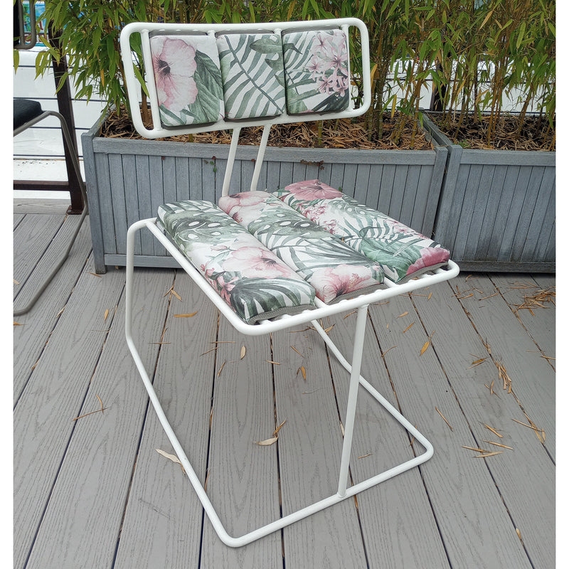 A comfortable Hope Chair by Egoe, featuring a tropical-themed cushion with green palm leaves and pink flowers, sits on a wooden deck. The background showcases tall planters with bamboo plants for an inviting oasis.