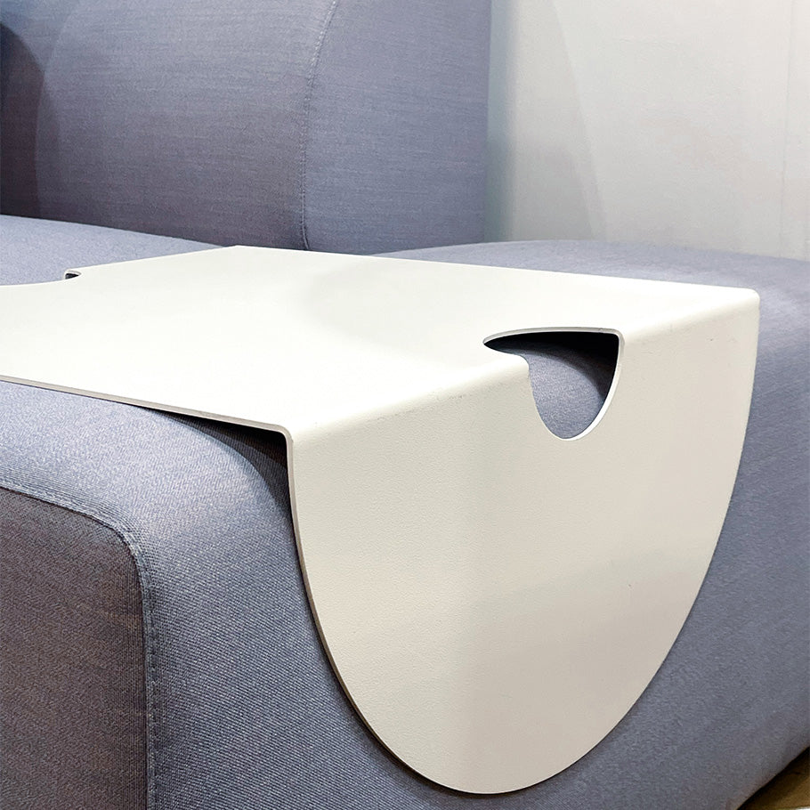 The Objekte unserer Tage Weber Modular Sofa features a modern white tray with a wavy design, crafted with German precision. It securely fits over the sofa arm and includes a cut-out handle, adding style and functionality to the minimalist setting.