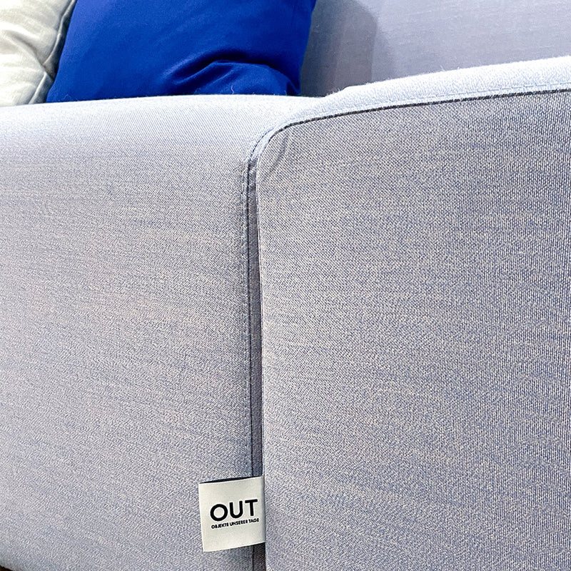 A close-up of the Weber Modular Sofa in light gray fabric with a blue cushion shows its texture and stitching, reflecting the German craftsmanship of Objekte unserer Tage. A small OUT label is near the armrest, emphasizing quality and sustainability.