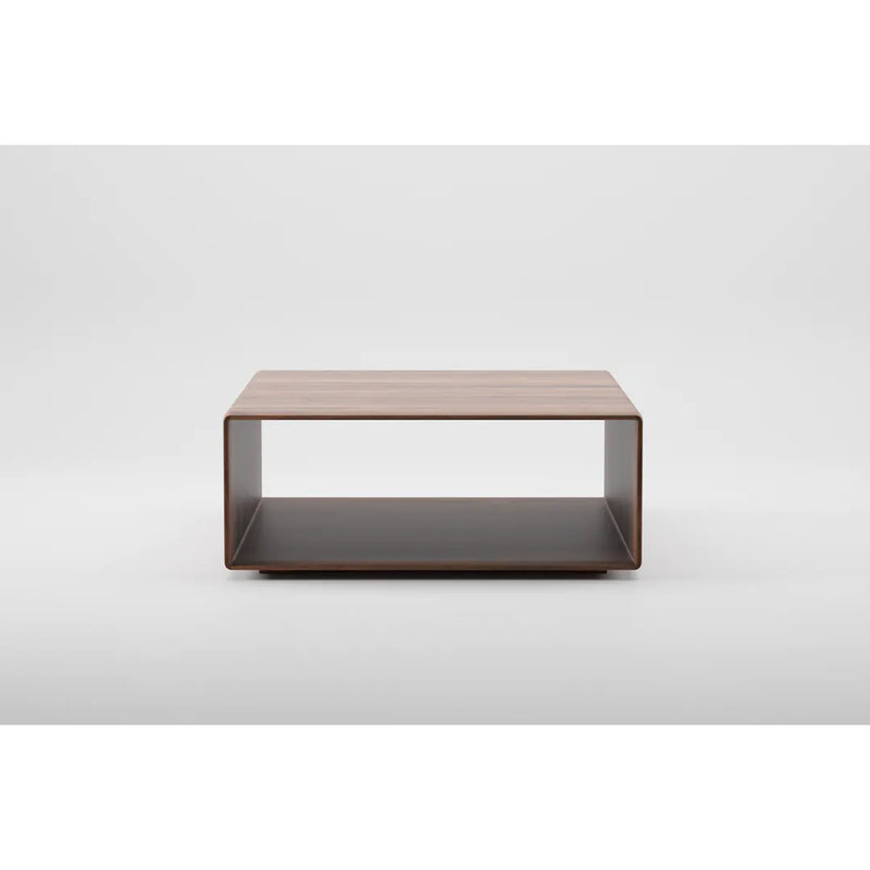 The INVITO Cube Coffee Table by Artisan is a sleek, minimalist piece made of solid wood with a natural oil finish. It has an open shelf and stands on a flat base. Its eco-friendly design is highlighted against a plain white background.