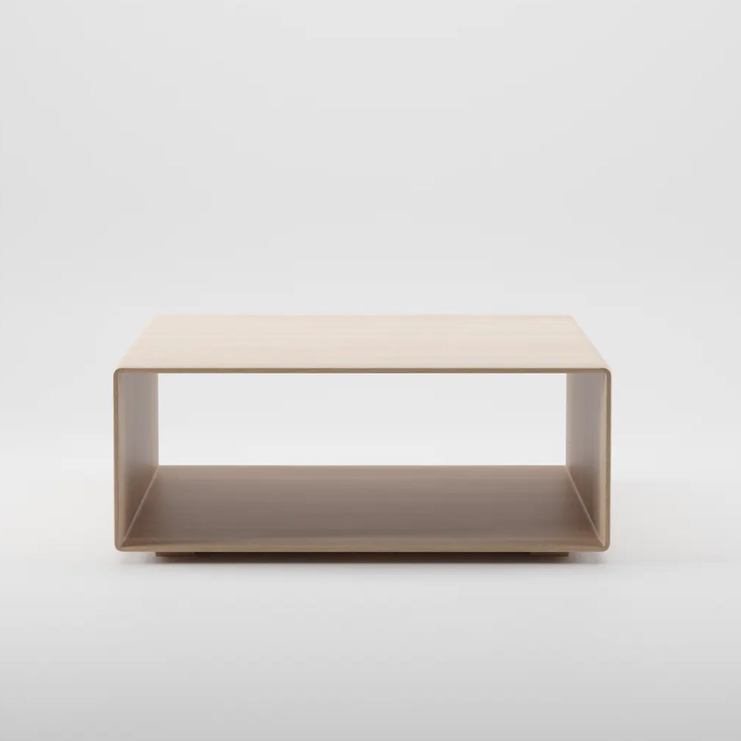 The INVITO Cube Coffee Table by Artisan is a minimalist piece made from solid wood with a light finish, featuring a rectangular design with open sides. It has a smooth surface enhanced with natural oils, elegantly wrapping around to form an integrated bottom shelf.