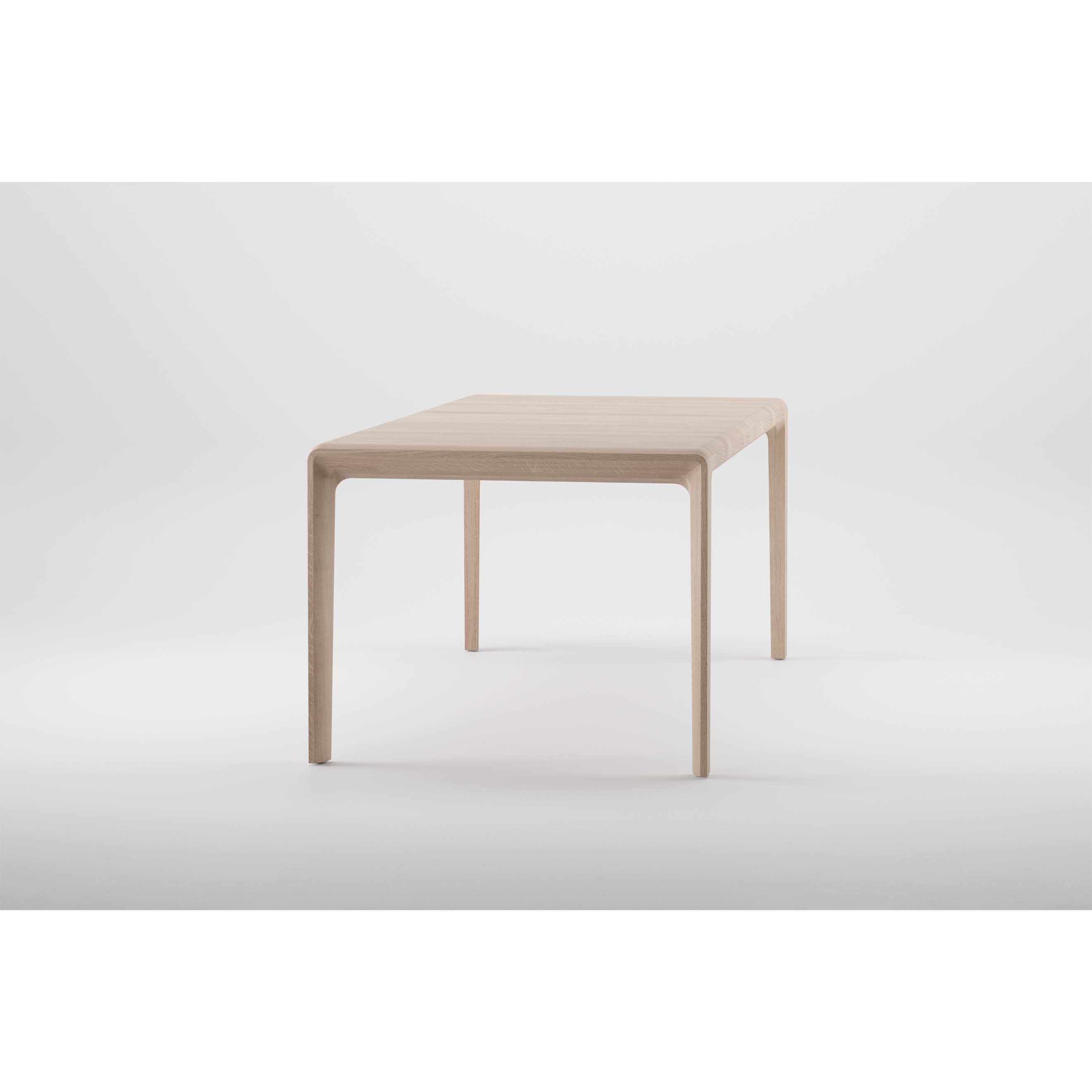 The Artisan INVITO Table is a minimalist, light wood table made from solid, eco-friendly materials. It has a smooth, rectangular top supported by four slender legs and is showcased against a plain light gray background.