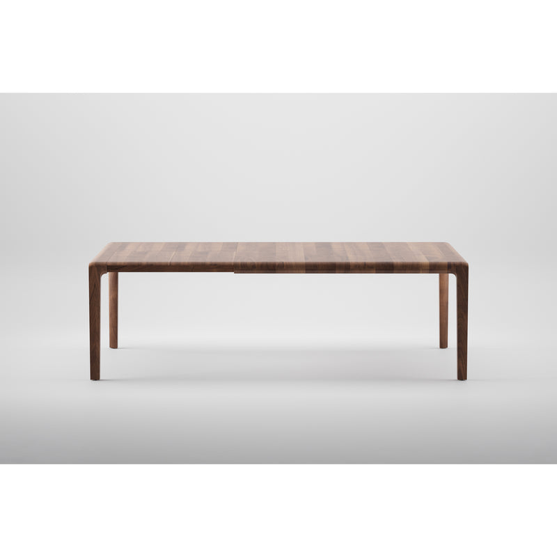 The Artisans INVITO Table Extendable is a minimalist wooden piece crafted from eco-friendly materials. It features a rectangular top with straight legs in a dark finish, using natural oils for an elegant look with no visible joints or decorations against a plain white background.