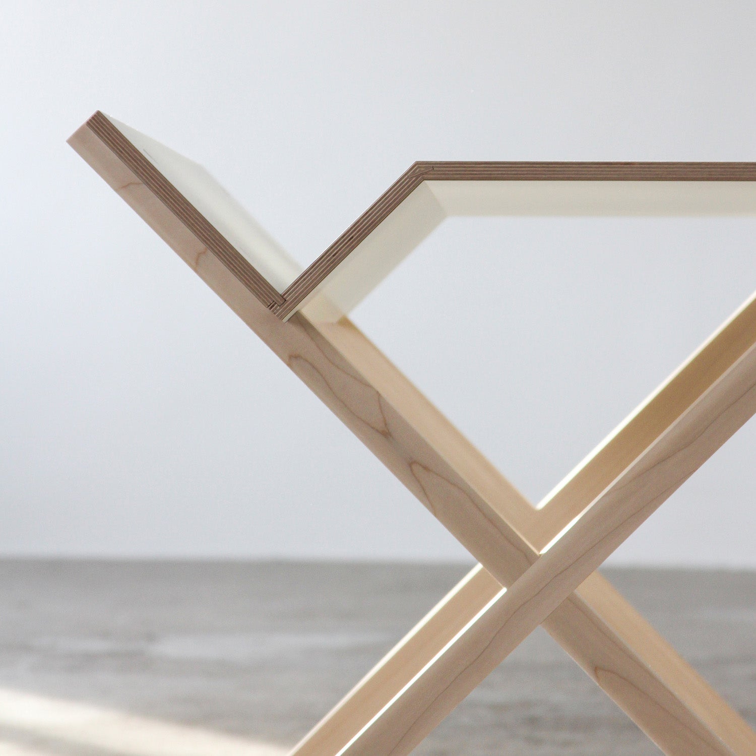 The Kant table by Moormann features a sleek glass top and wooden X-shaped legs, ideal for an organized desk space. The photo highlights the corner, showcasing its clean lines and minimalist design against a neutral backdrop.