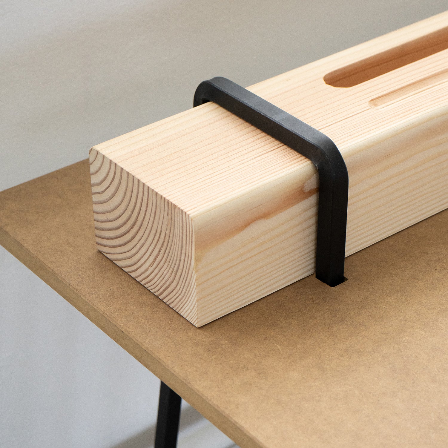 A light wooden beam with a rectangular slot, secured to the tabletop by a black metal clamp, is reminiscent of Moormanns Kurt. The brown table surface contrasts with the wood grain, cleverly suggesting concealed storage space.