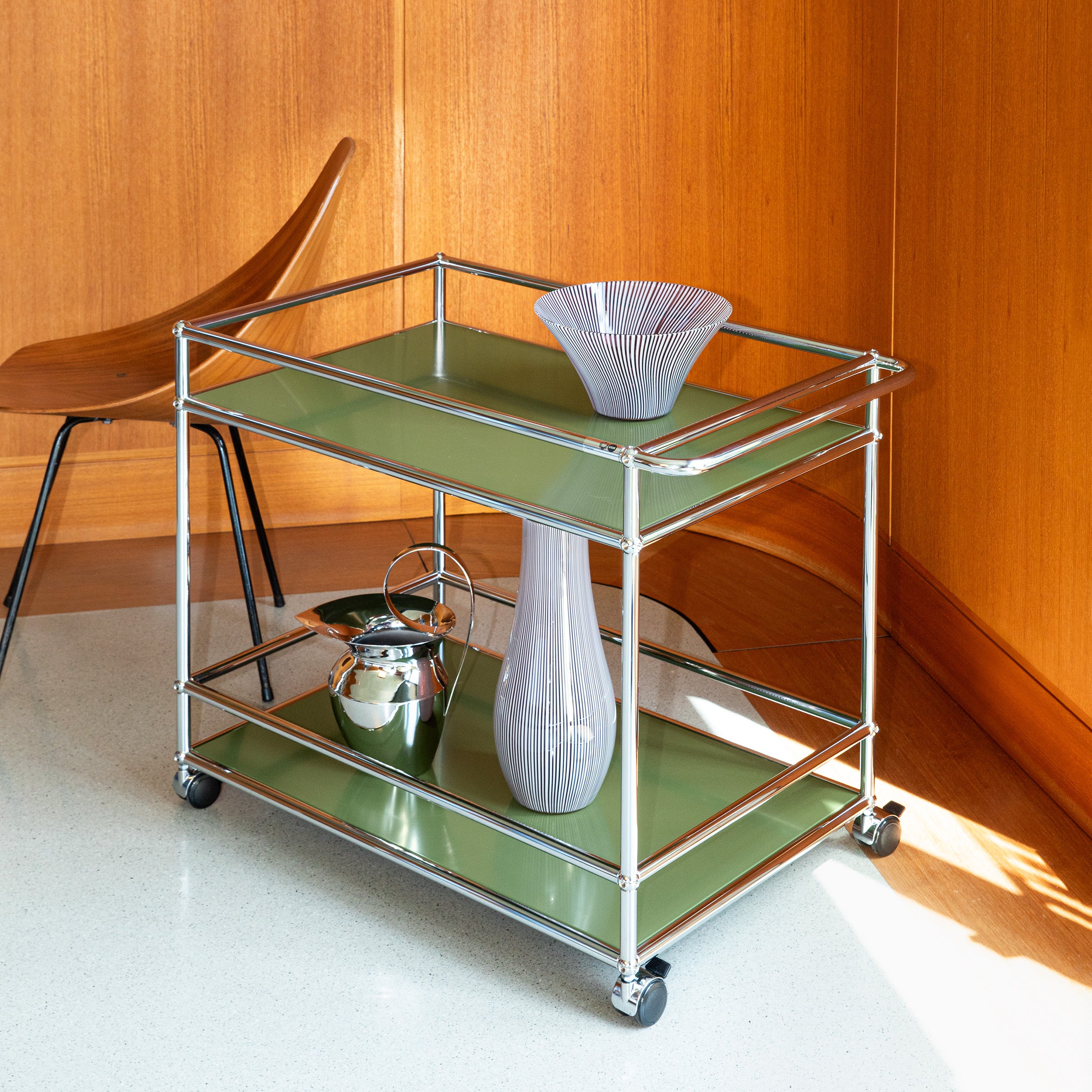 Haller Serving Cart L18 in olive green with chrome frame and casters holding decorative vases in modern room corner.