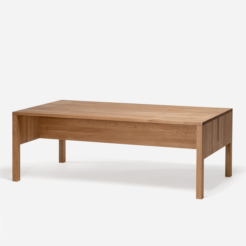 The L8 Traba Table by Loehr is a minimalist rectangular coffee table crafted from solid light brown wood. It features straight lines, natural wood grain, four sturdy legs, and comes in various finishes that highlight its structural rigidity and elegant simplicity against the clean background.