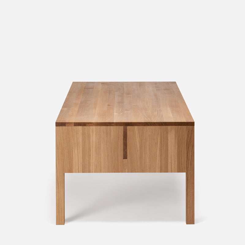The L8 Traba Table by Loehr, featuring a minimalist design and natural wood finish with straight legs, is centered against a plain white background. It offers structural rigidity and exudes a simple, clean look.