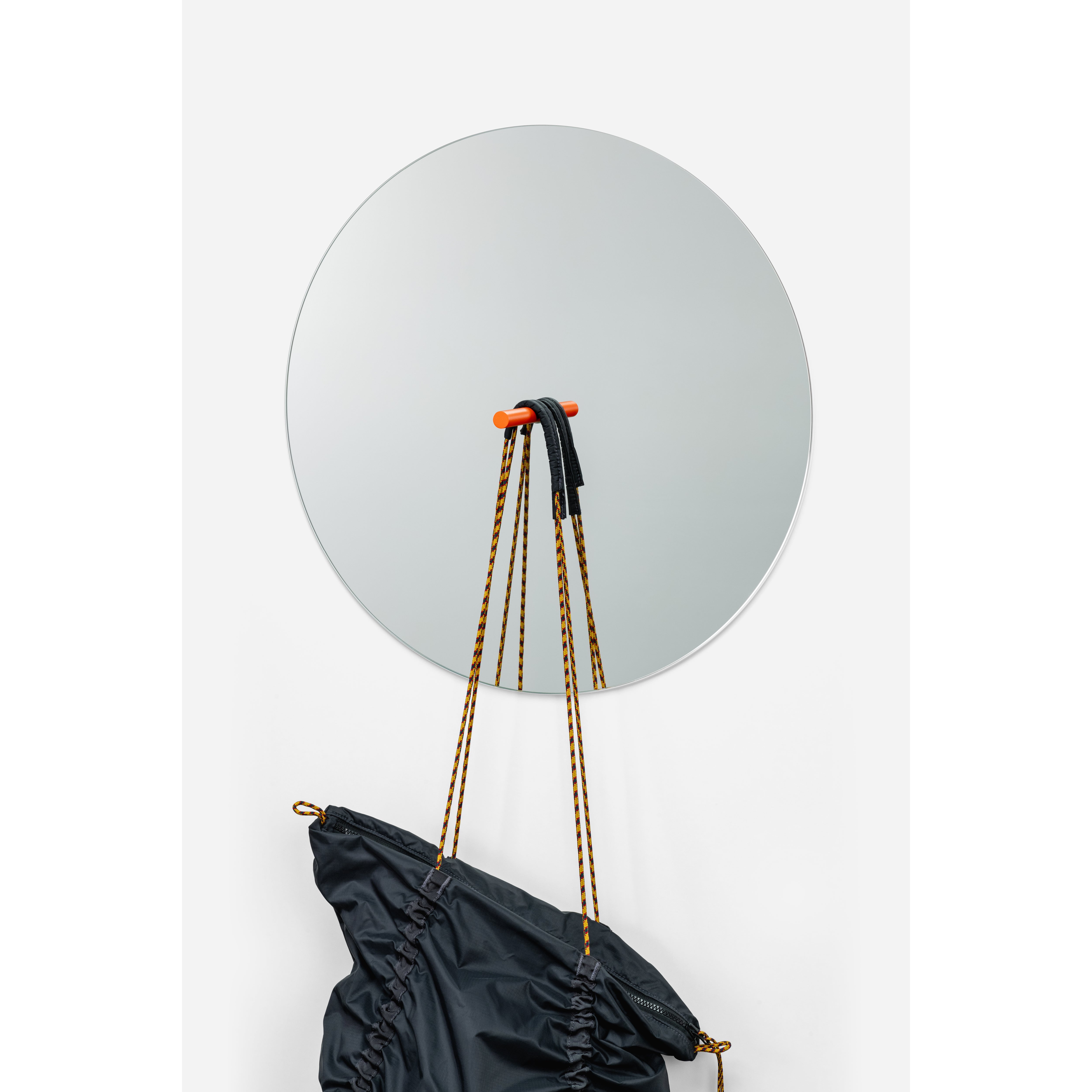 The L9 Portal by Loehr serves as a chic decorative piece on the wall, featuring a drawstring bag hanging from a red hook. The mirrors surface highlights the bags black and yellow straps, forming an elegant style portal.